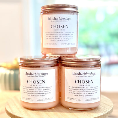 Three blush pink wax melt jars with copper lids are stacked on a round wooden pedestal. The top jar  is centered, with two matching jars below it. Labels say "Chosen" and have John 15:16 written out. 